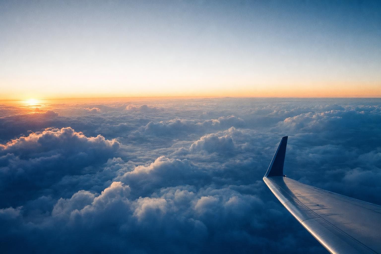 Airplane wing above clouds at sunrise